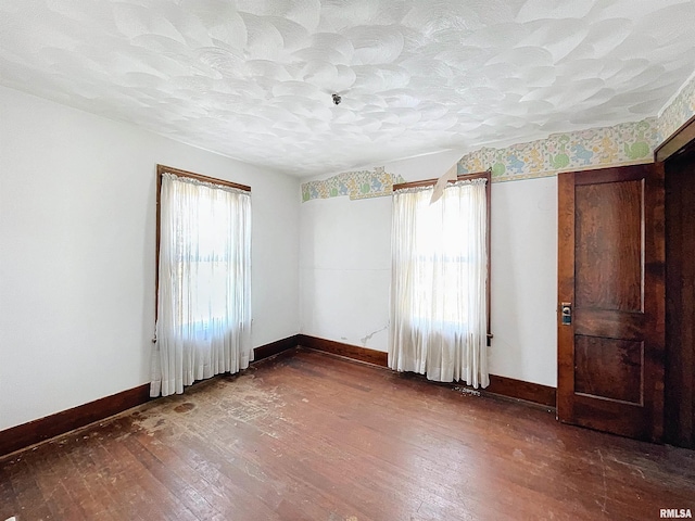 unfurnished room with a textured ceiling, plenty of natural light, and dark wood-type flooring