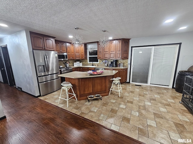 kitchen featuring appliances with stainless steel finishes, tasteful backsplash, a kitchen bar, hanging light fixtures, and a center island