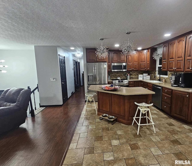 kitchen with a kitchen island, appliances with stainless steel finishes, pendant lighting, sink, and a kitchen breakfast bar