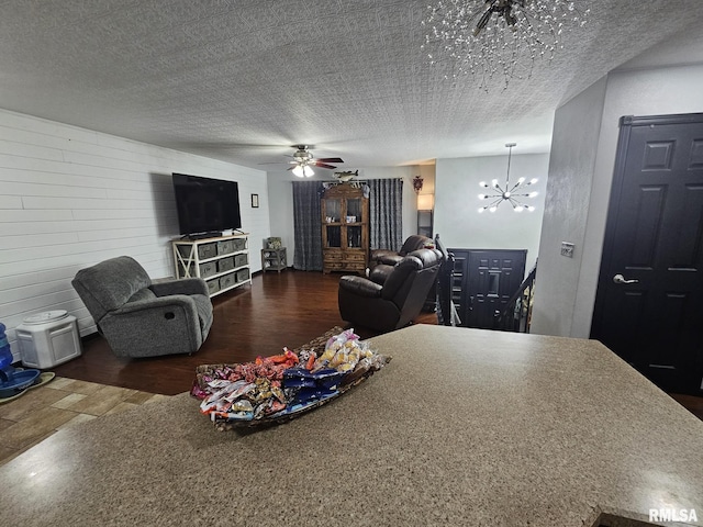 living room with dark wood-type flooring, ceiling fan with notable chandelier, and a textured ceiling