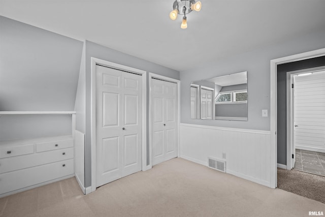 unfurnished bedroom featuring light carpet and multiple closets