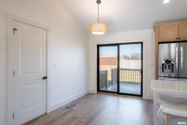 unfurnished dining area featuring vaulted ceiling and light hardwood / wood-style flooring