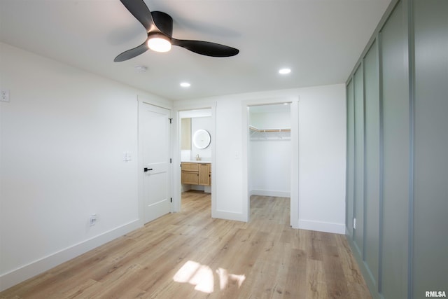 unfurnished bedroom featuring ceiling fan, connected bathroom, a closet, a walk in closet, and light hardwood / wood-style flooring