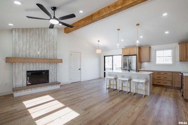 kitchen with a kitchen island, backsplash, stainless steel fridge, a large fireplace, and ceiling fan