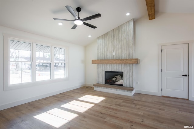 unfurnished living room featuring light wood-type flooring, ceiling fan, a large fireplace, and vaulted ceiling with beams