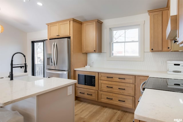 kitchen featuring stainless steel refrigerator with ice dispenser, backsplash, black microwave, light hardwood / wood-style flooring, and sink