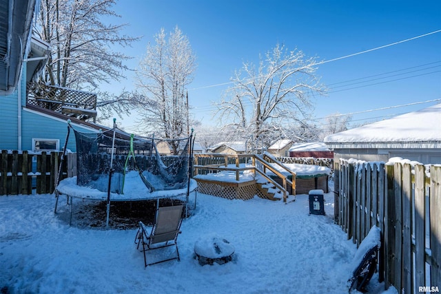 snowy yard featuring a trampoline and a wooden deck