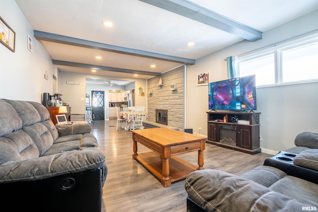 living room with a fireplace, beam ceiling, light hardwood / wood-style floors, and ceiling fan