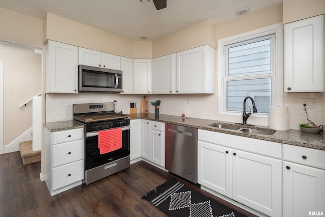 kitchen with appliances with stainless steel finishes, white cabinetry, dark stone counters, and sink