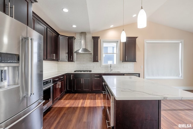 kitchen with a center island, lofted ceiling, backsplash, wall chimney range hood, and appliances with stainless steel finishes