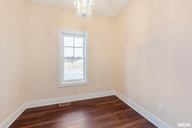 spare room with a notable chandelier and dark wood-type flooring