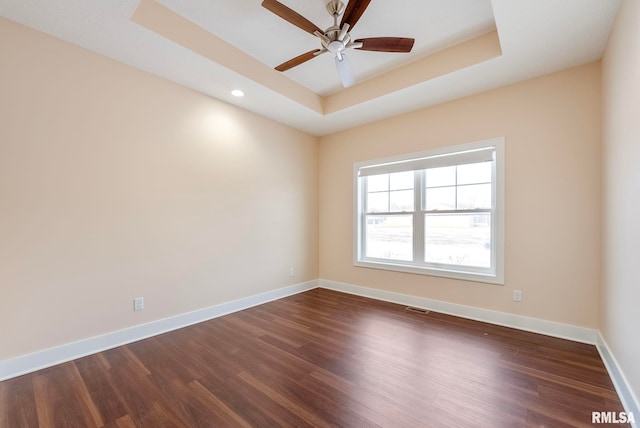 empty room with dark hardwood / wood-style flooring, ceiling fan, and a raised ceiling