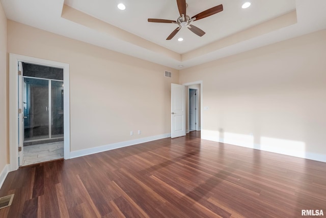 spare room featuring a raised ceiling, ceiling fan, and dark wood-type flooring