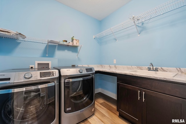 laundry area with cabinets, light wood-type flooring, a textured ceiling, sink, and washing machine and clothes dryer