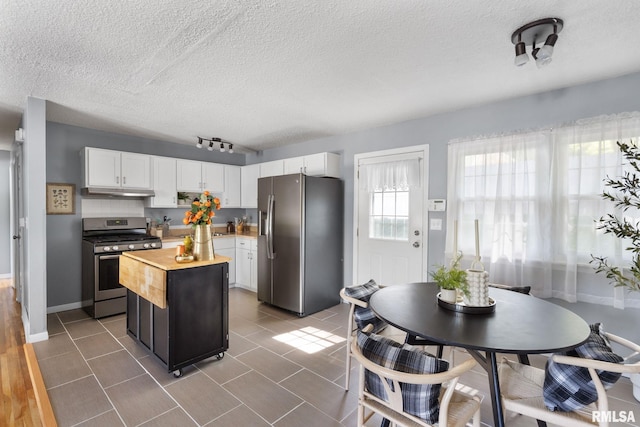 kitchen featuring appliances with stainless steel finishes, a kitchen island, dark tile patterned floors, butcher block countertops, and white cabinetry