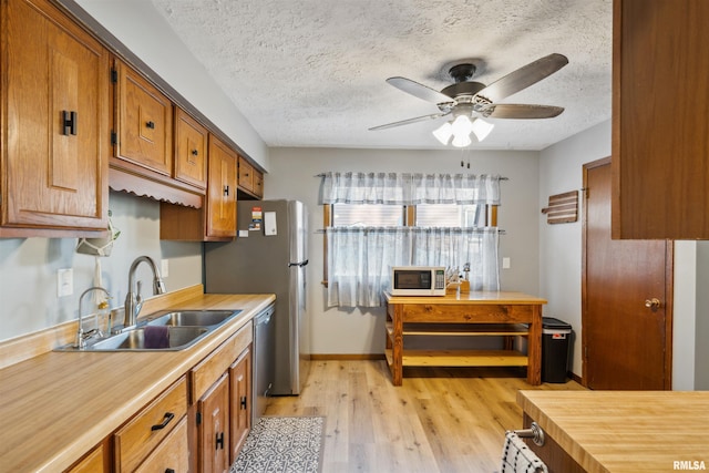 kitchen featuring sink, a textured ceiling, dishwasher, ceiling fan, and light hardwood / wood-style floors