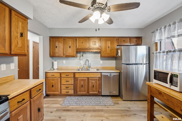 kitchen featuring a textured ceiling, light hardwood / wood-style flooring, stainless steel appliances, ceiling fan, and sink