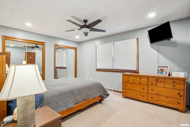 bedroom featuring a textured ceiling, light colored carpet, ceiling fan, and multiple closets