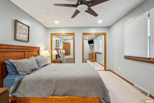 bedroom with two closets, ceiling fan, a textured ceiling, and light colored carpet