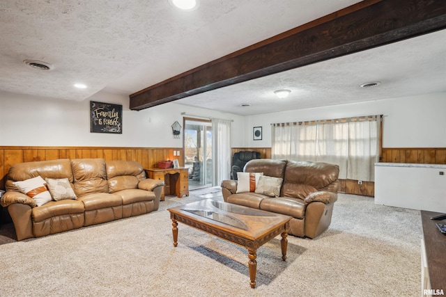 carpeted living room with wooden walls, a textured ceiling, and beam ceiling