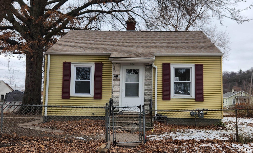 view of front of house with a fenced front yard, a chimney, a gate, and a shingled roof