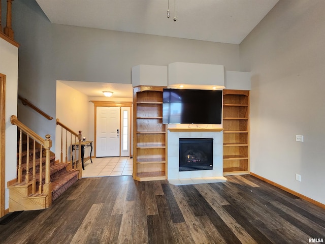 unfurnished living room featuring a tile fireplace, a towering ceiling, and hardwood / wood-style flooring