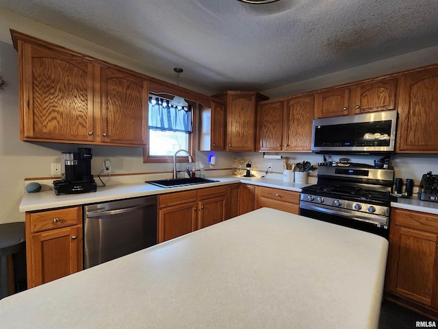 kitchen with a textured ceiling, sink, stainless steel appliances, and hanging light fixtures