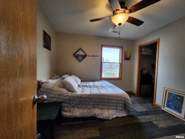 bedroom featuring a walk in closet, a closet, dark hardwood / wood-style floors, and ceiling fan