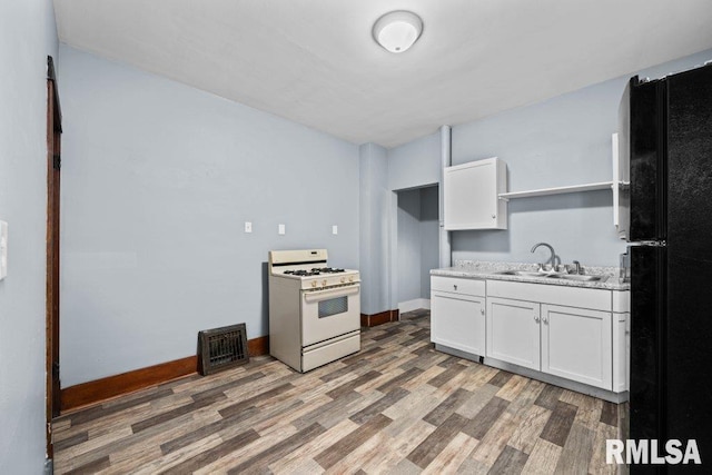 kitchen featuring black refrigerator, sink, white range with gas stovetop, dark hardwood / wood-style floors, and white cabinetry