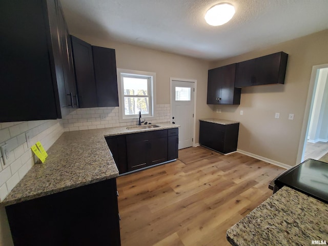 kitchen featuring light wood-type flooring, backsplash, light stone counters, and sink