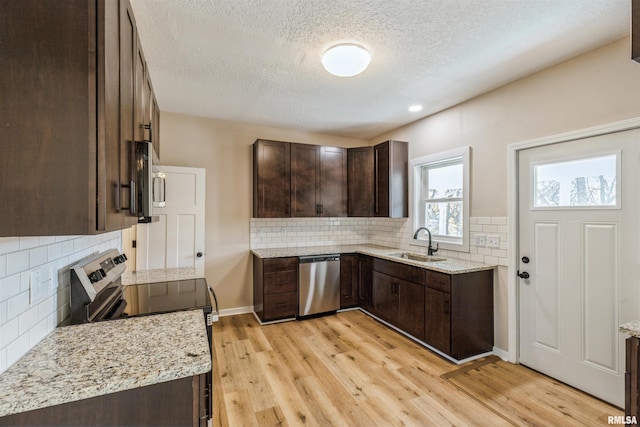 kitchen with dark brown cabinetry, light stone countertops, sink, appliances with stainless steel finishes, and light wood-type flooring