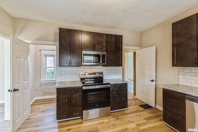 kitchen with dark brown cabinetry, stainless steel appliances, light stone counters, and light hardwood / wood-style flooring