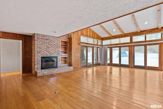 unfurnished living room with a wealth of natural light, wooden walls, and a fireplace