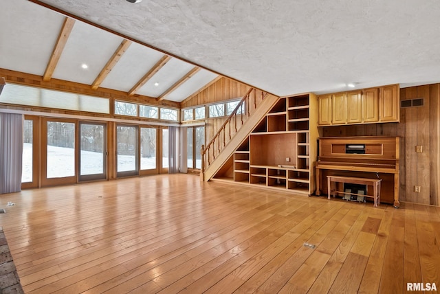 unfurnished living room featuring light hardwood / wood-style floors, wood walls, and vaulted ceiling with beams