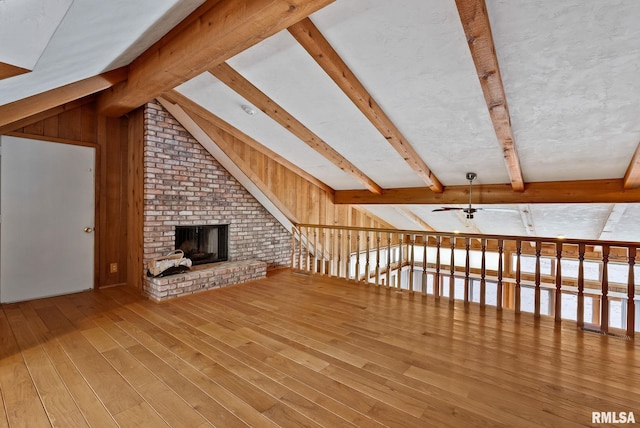 unfurnished living room featuring hardwood / wood-style floors, wooden walls, ceiling fan, a fireplace, and lofted ceiling with beams