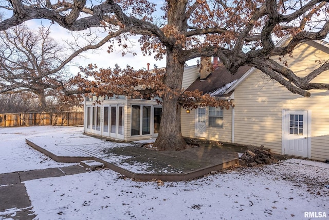 snow covered rear of property featuring a sunroom