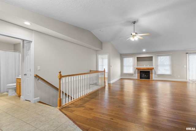 unfurnished living room with a textured ceiling, ceiling fan, light hardwood / wood-style floors, lofted ceiling, and a tiled fireplace