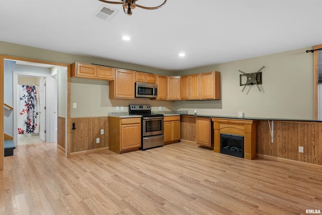 kitchen with wood walls, light wood-type flooring, and appliances with stainless steel finishes