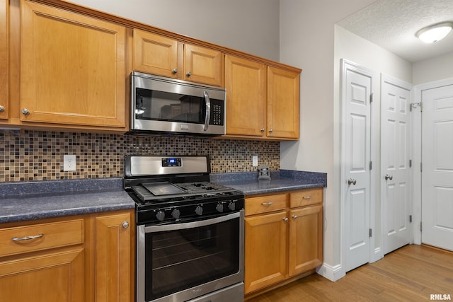 kitchen featuring a textured ceiling, stainless steel appliances, tasteful backsplash, and light hardwood / wood-style floors