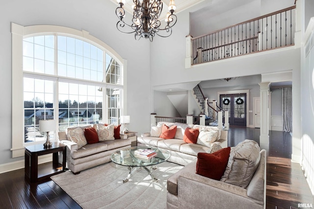 living room featuring a towering ceiling, dark hardwood / wood-style floors, ornate columns, and an inviting chandelier