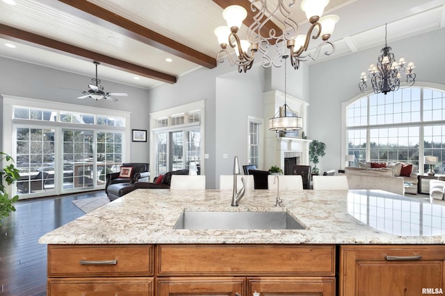 kitchen with sink, hanging light fixtures, ceiling fan, beamed ceiling, and light stone counters