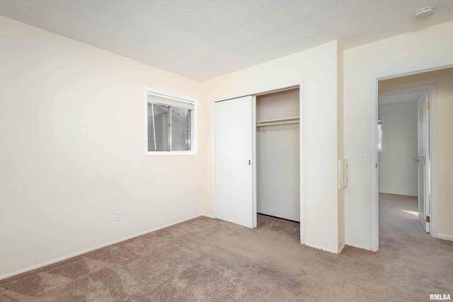 unfurnished bedroom featuring a textured ceiling, a closet, and light carpet