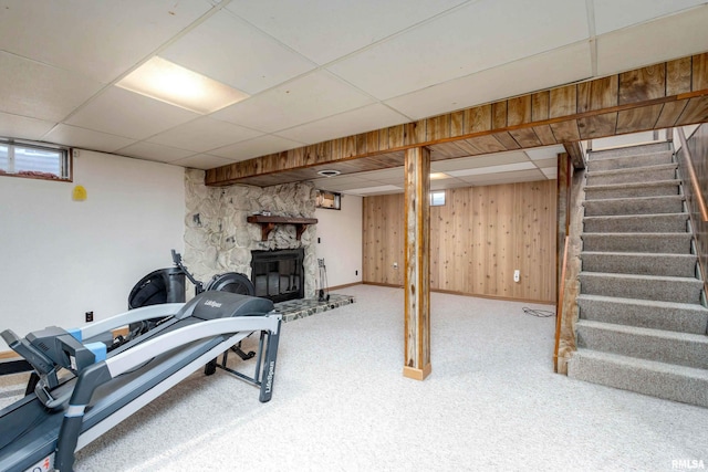 workout area featuring carpet flooring, wooden walls, a paneled ceiling, and a stone fireplace