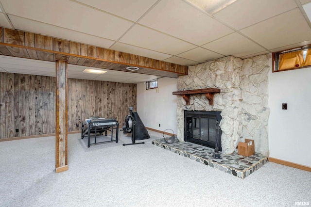 basement featuring a stone fireplace, carpet, wood walls, and a drop ceiling