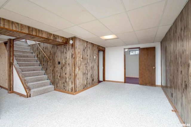 basement featuring a paneled ceiling, wood walls, and carpet