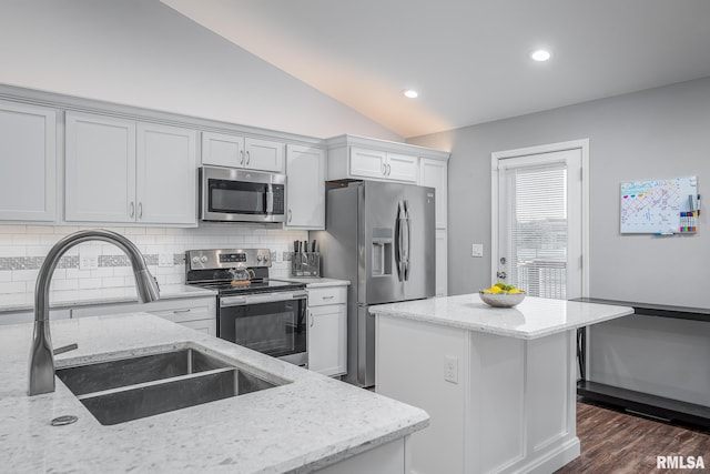 kitchen with lofted ceiling, sink, light stone counters, and appliances with stainless steel finishes