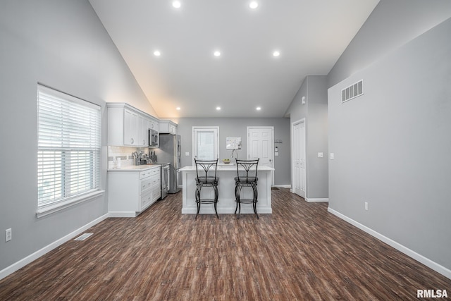 kitchen with dark wood-type flooring, stainless steel appliances, a kitchen island, backsplash, and a kitchen breakfast bar