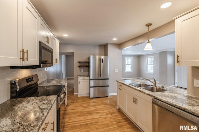 kitchen featuring light wood finished floors, appliances with stainless steel finishes, hanging light fixtures, white cabinetry, and a sink