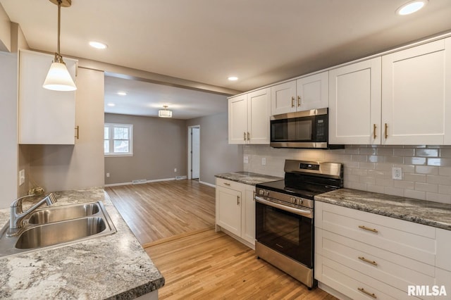 kitchen with tasteful backsplash, white cabinets, appliances with stainless steel finishes, pendant lighting, and a sink