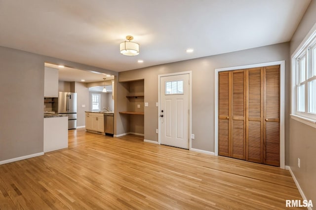 unfurnished living room with light wood-style floors, recessed lighting, a sink, and baseboards